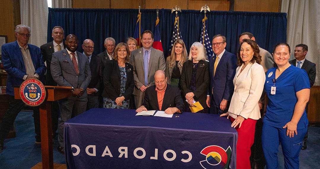 Governor Polis signing HB24-1231 surrounded by supporters of the proposed College of Osteopathic Medicine.